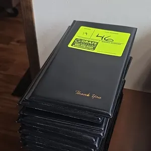 Padded restaurant check presenters. Features black vinyl exterior with gold-foil stamped "Thank You" script, interior credit card pocket, and receipt 