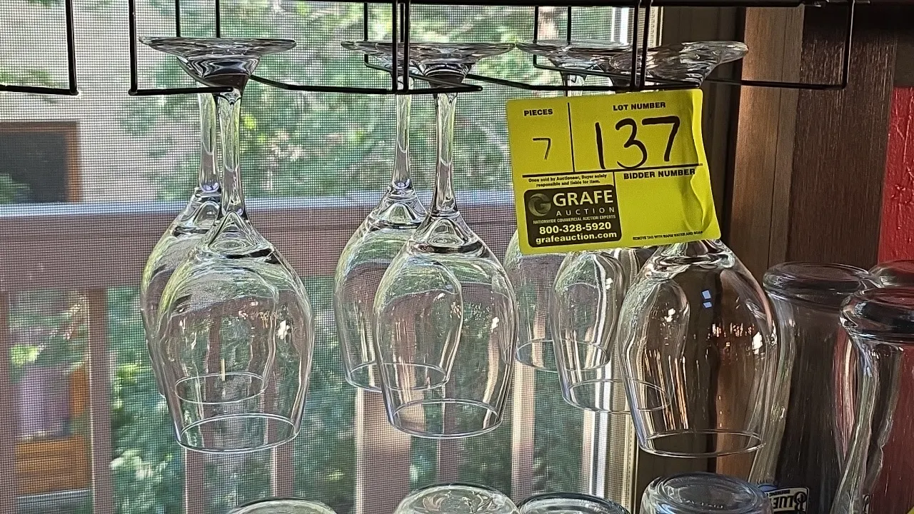 Stemmed wine glasses. Features clear glass construction with round bases and tapered bowls. Note: Hanging rack and background glassware not included.