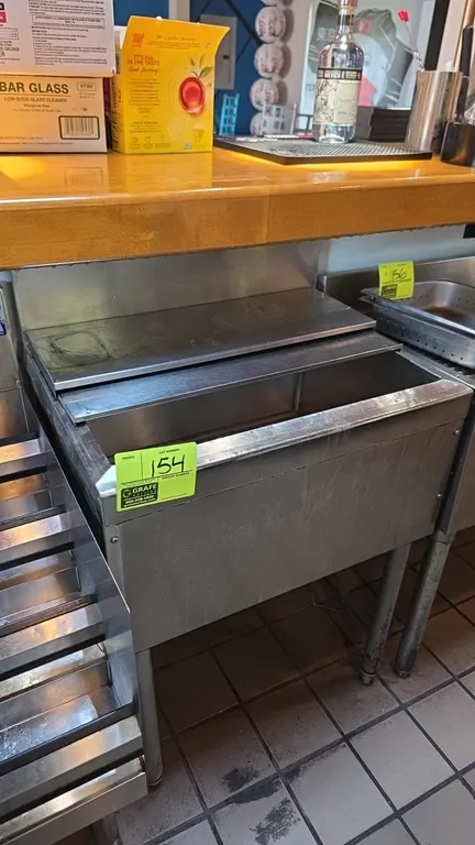 Stainless steel undercounter ice bin. Features an integrated backsplash, sliding stainless steel cover, and center drain. 24" x 18". Mounted on tubula