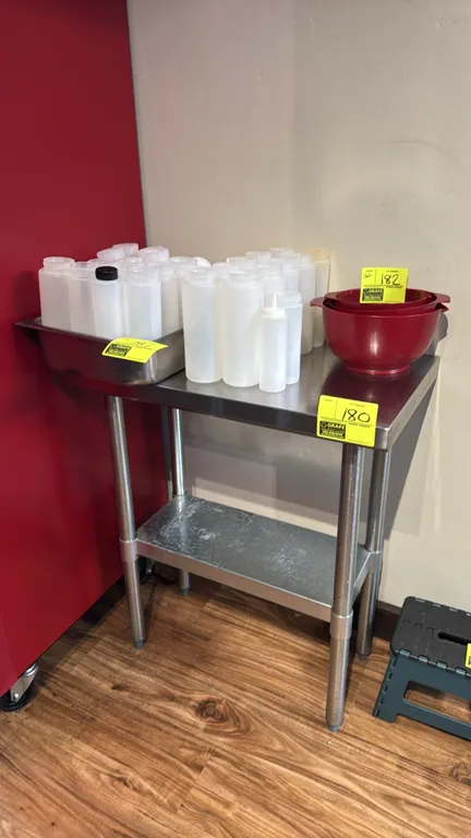 Stainless steel work table. Features a galvanized undershelf and tubular legs with adjustable bullet feet. Dimensions: 30"L x 18"W x 35"H. Contents no