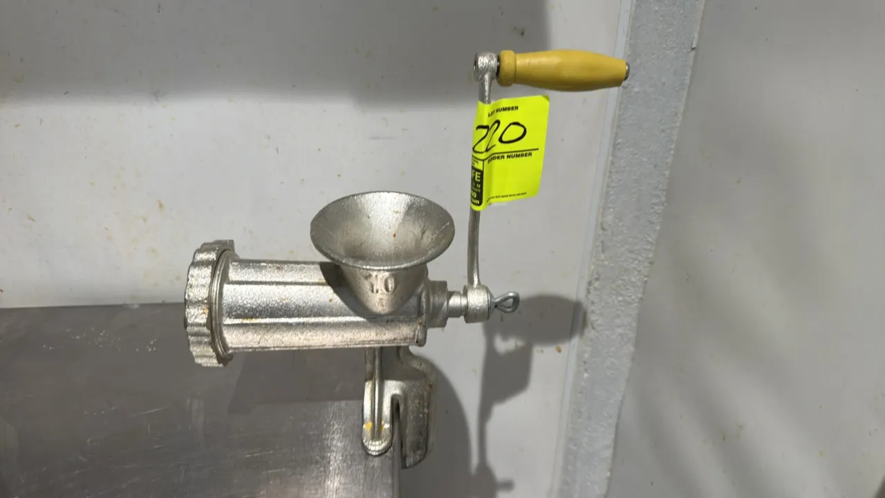 Cast metal manual meat grinder. Features size No. 10 body, hand crank with yellow handle, grinding plate with screw collar, and integrated table clamp