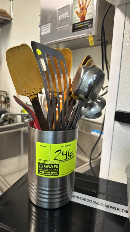 Assorted commercial kitchen utensils with stainless steel cylinder holder. Includes silicone scrapers and spatulas, slotted metal turner, and stainles
