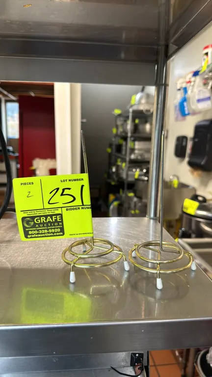 Metal ticket holders. Features brass-tone wire construction, upright spindle receipt spikes, tiered circular bases, and protective rubber feet.