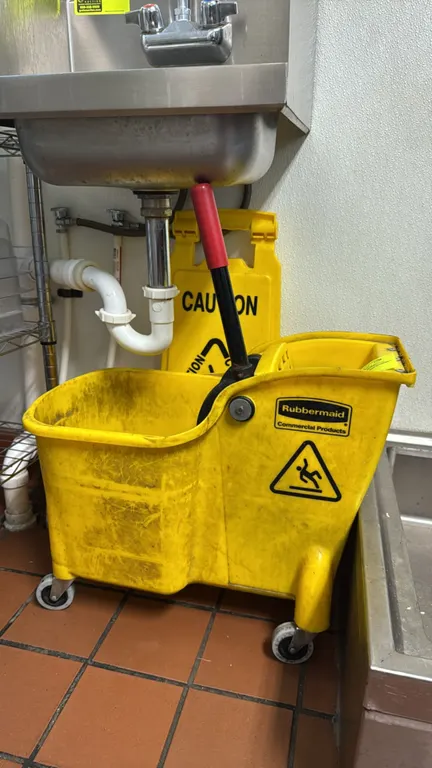Rubbermaid mop bucket with wringer and wet floor sign. Features yellow polyethylene construction and wringer with handle. Mounted on swivel casters. I