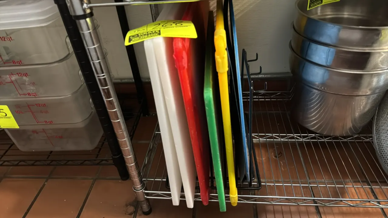 Assorted polyethylene cutting boards with wire storage rack. Includes (2) white boards, (1) red board, (1) green board, (1) yellow board with corner g