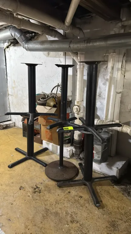 Metal pedestal table bases. Features black finished metal construction with central columns, top mounting plates, and assorted base designs including