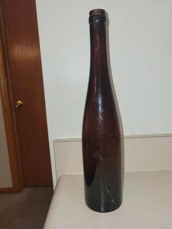 tall, slender amber-brown glass bottle with a long, tapering neck and a rounded lip, resembling a vi
