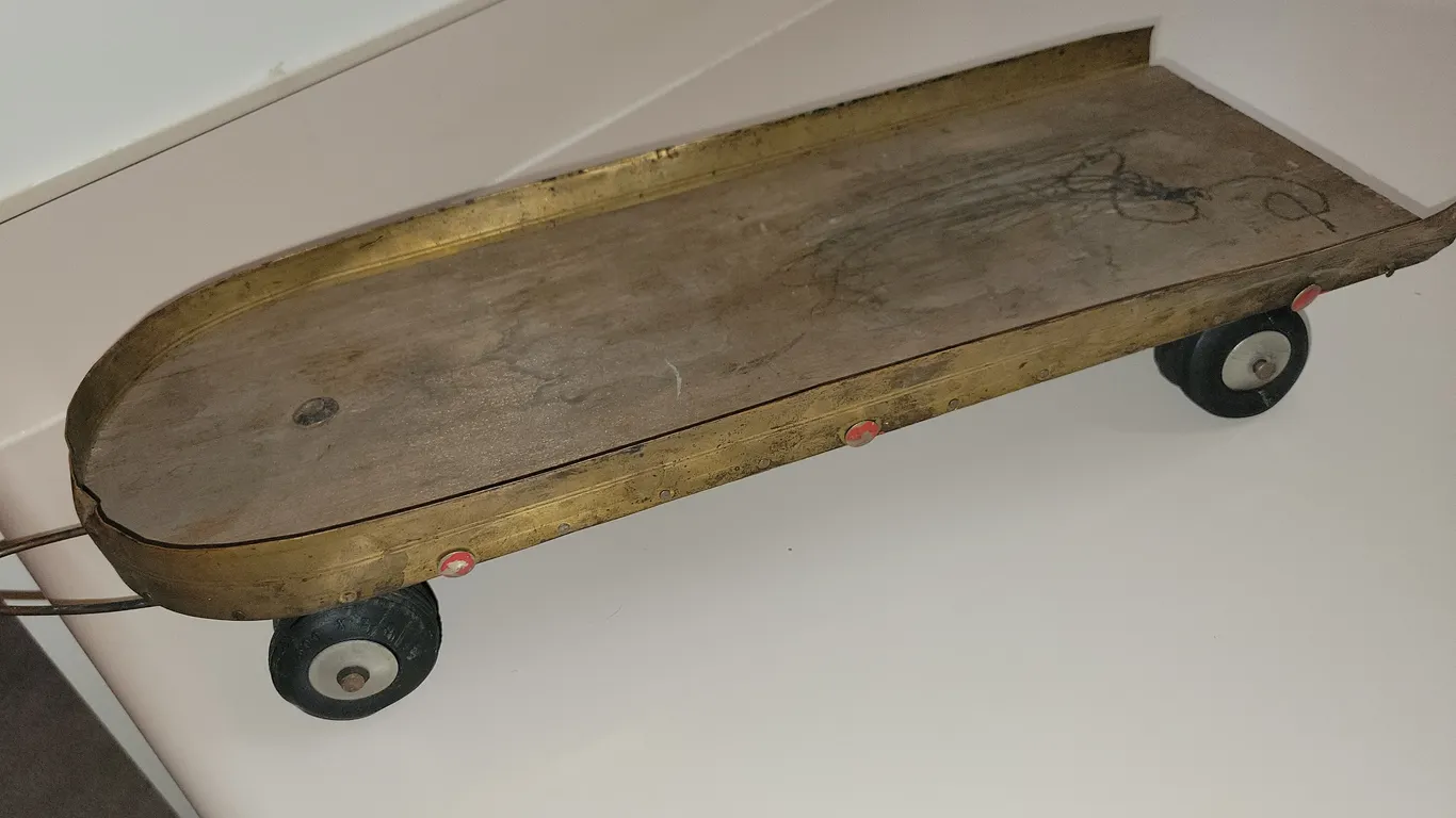 vintage hand-crafted or early wheeled toy with a long, metallic or brass-toned wooden-backed board r