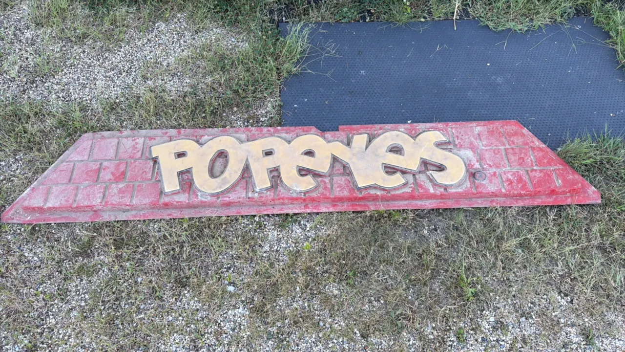 Popeyes restaurant sign section, red with gold raised letters and brick texture