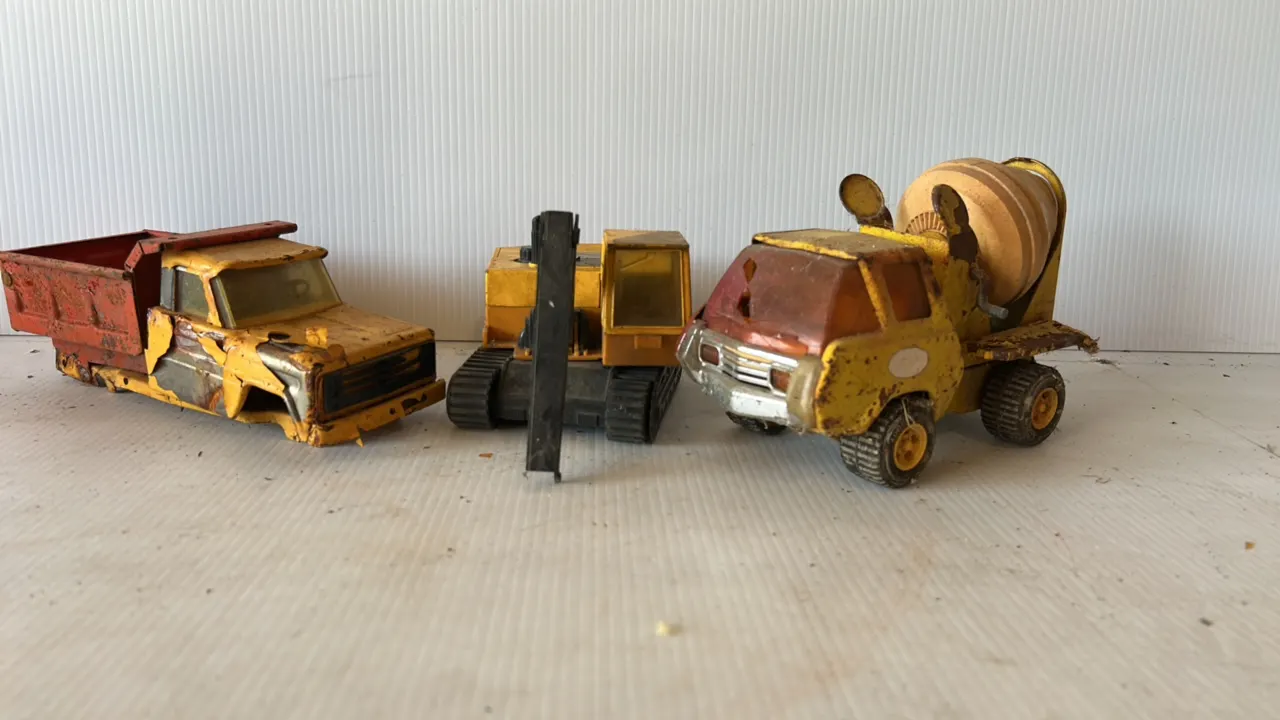 Set of three vintage metal toy construction vehicles, including a dump truck, excavator, and cement mixer