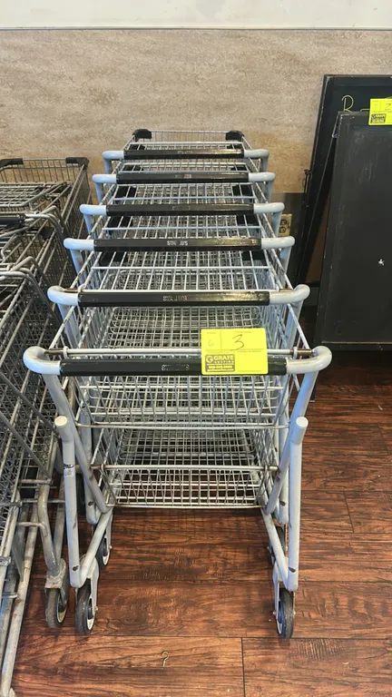 Two-tier metal wire shopping carts. Features upper and lower wire baskets, tubular metal frame, corner bumpers, plastic handle grips, and nesting desi