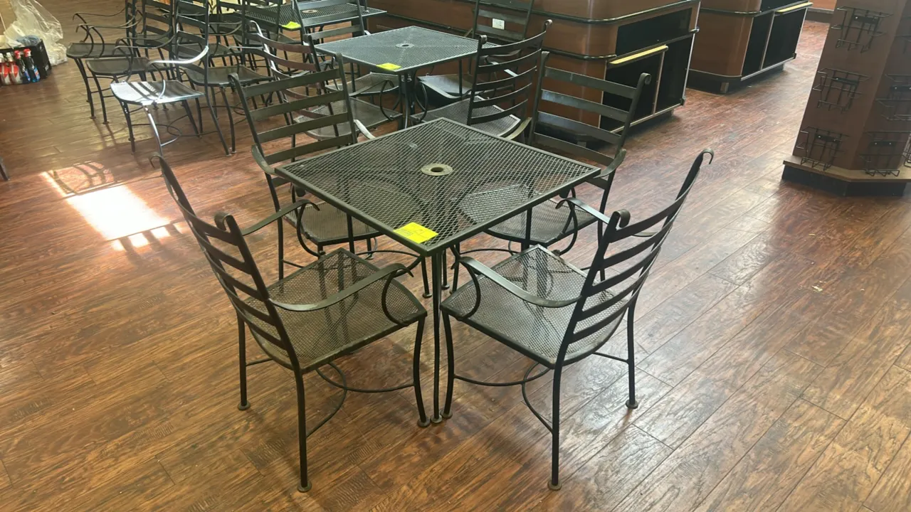Metal patio dining table with (4) matching armchairs. Table features a square mesh top with center umbrella hole and curved metal legs. Chairs feature