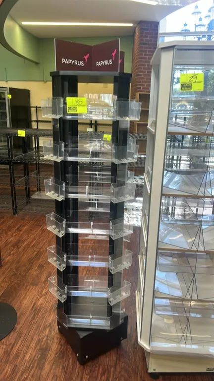 Papyrus 4-sided rotating merchandiser display rack. Features black laminate construction, multi-tier clear acrylic pockets, and Papyrus branded header