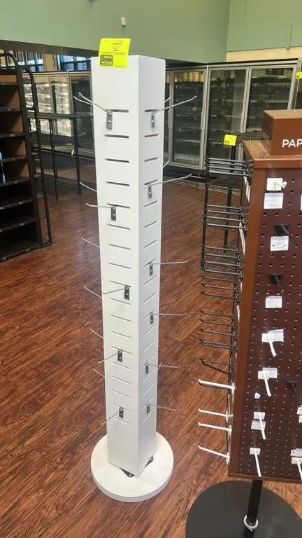 4-sided rotating floor display merchandiser. Features white laminate construction, slotted display panels with wire hooks, and a circular rotating bas