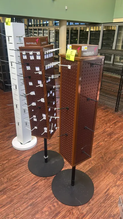 Papyrus 4-sided rotating pegboard merchandisers. Features brown laminate construction, 4-sided perforated pegboard panels, branded header blocks, and