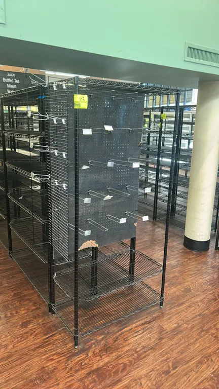 Metal wire 2-sided display merchandiser. Features black wire construction, center pegboard with peg hooks, and lower wire shelves. 42" x 18". Note: Ce