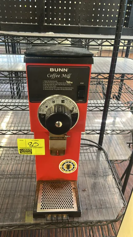 Bunn G1 HD bulk coffee grinder. Features multi-position grind selector dial, bag clamp chute with cleaning lever, perforated catch tray, and red finis