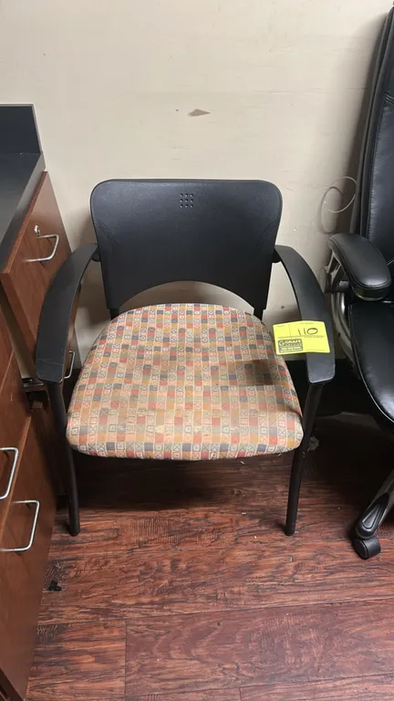 Armchair. Features a black molded polypropylene backrest, patterned fabric cushioned seat, and fixed armrests. Mounted on a black metal four-leg base.