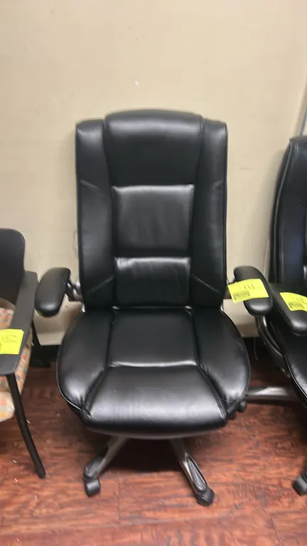 High-back executive office chair. Features black faux leather cushioned upholstery, high backrest, and padded armrests. Mounted on a 5-star swivel bas