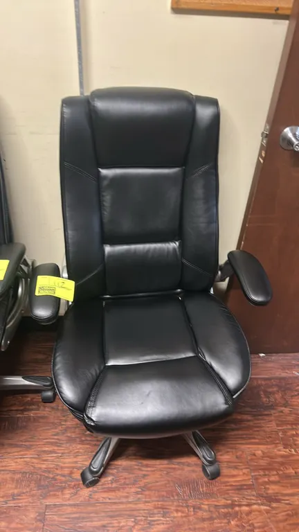 High-back executive office chair. Features black upholstered segmented cushioning, integrated headrest, and padded armrests. Mounted on a 5-star swive