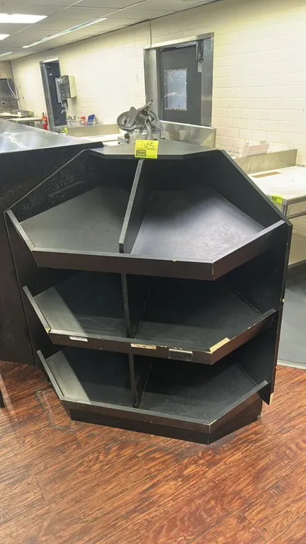 3-tier laminate merchandiser display fixture. Features black laminate construction, 3-tier angled display shelving with vertical center dividers, and