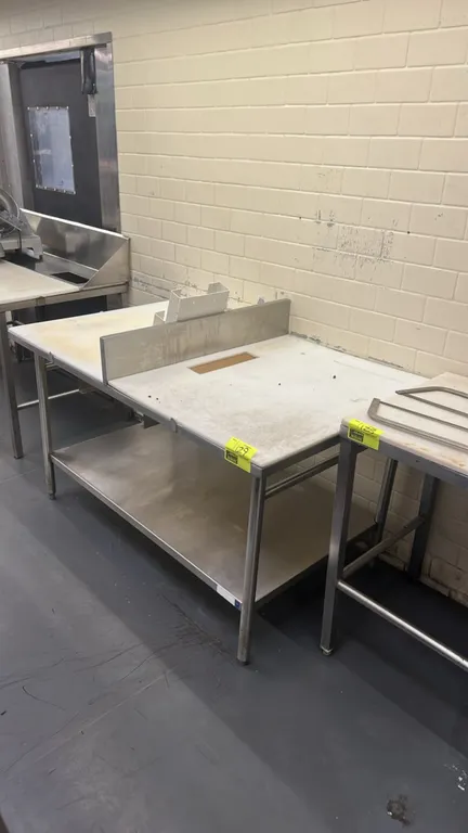 Stainless steel work table. Features poly cutting board top with scrap cutout, center stainless steel divider with holder, and full stainless steel un