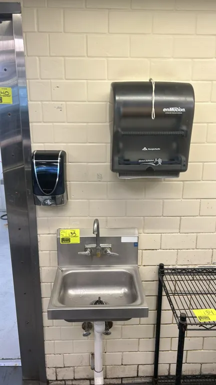 Stainless steel handwashing sink. Features an integrated backsplash, splash-mount gooseneck faucet with dual lever handles, and basket strainer drain.
