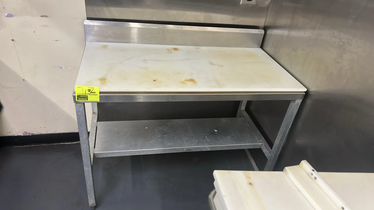 Stainless steel work table. Features a removable poly top cutting board surface, integrated backsplash, and lower undershelf. 4' x 2'. Mounted on squa