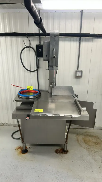 Hobart stainless steel meat saw. Features sliding carriage table, adjustable thickness gauge plate, and lower catch pan. Mounted on adjustable levelin