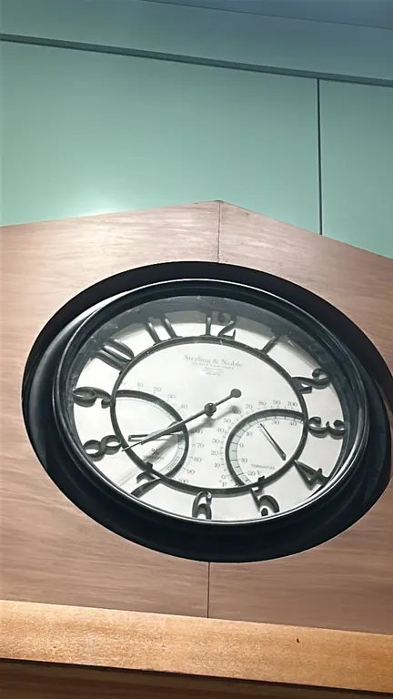 Sterling & Noble analog wall clock. Features dark circular bezel, raised-style Arabic numerals, and integrated thermometer and hygrometer sub-dials. S