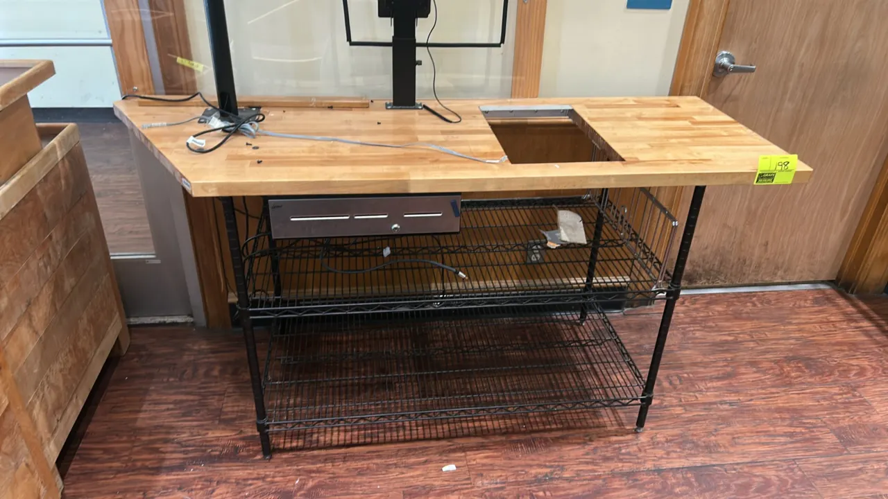 Checkout counter work table. Features a 6'x2' wooden butcher block top with equipment cutout, undercounter cash drawer, and monitor mounting brackets.