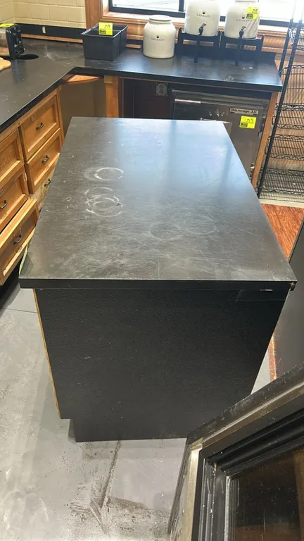 Laminate top service counter cabinet. Features black laminate top, open-face wooden vertical divider compartments, and black exterior casing. Dimensio