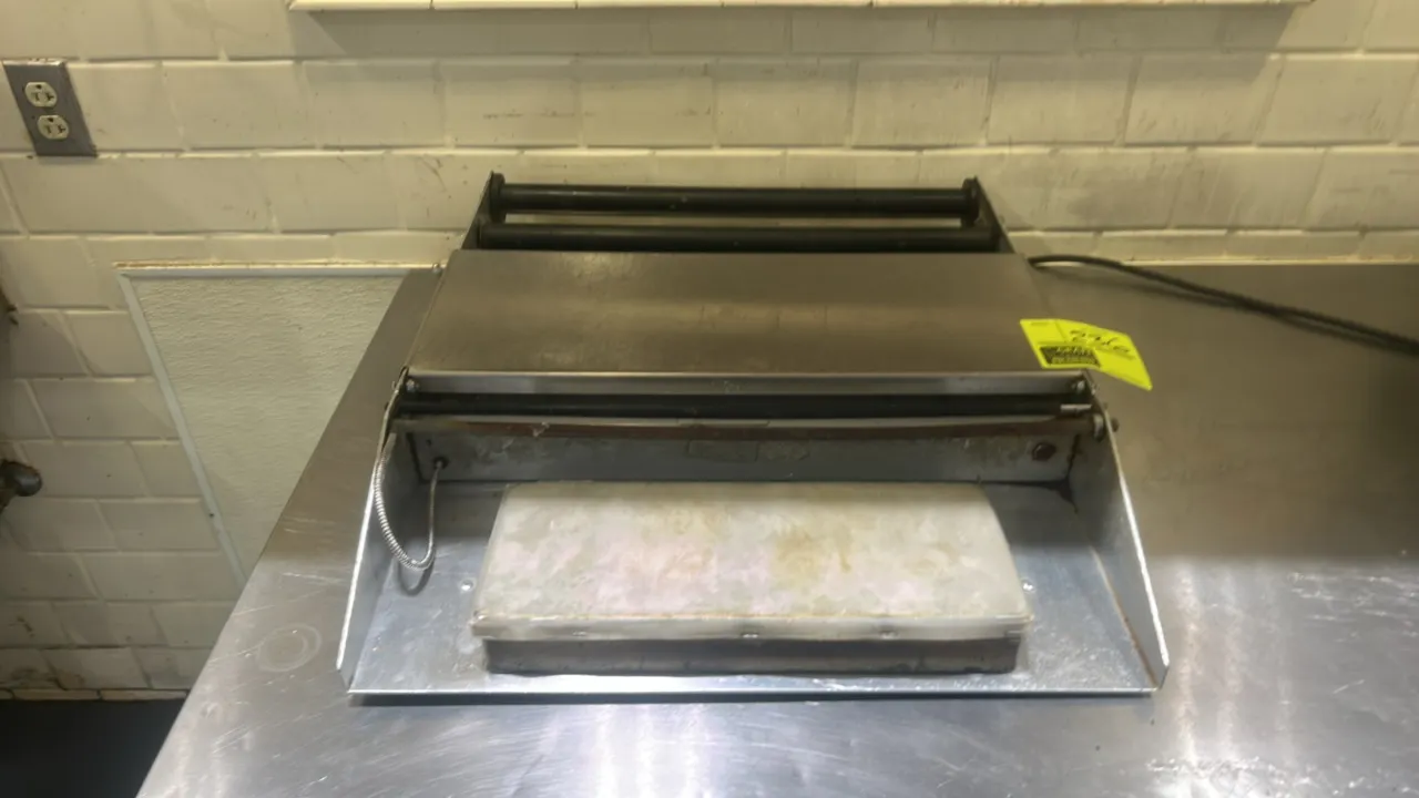 Heat Seal stainless steel film wrapper. Features integrated hot plate seal pad, film roll cradle rollers, cut-off bar, and countertop design. Electric