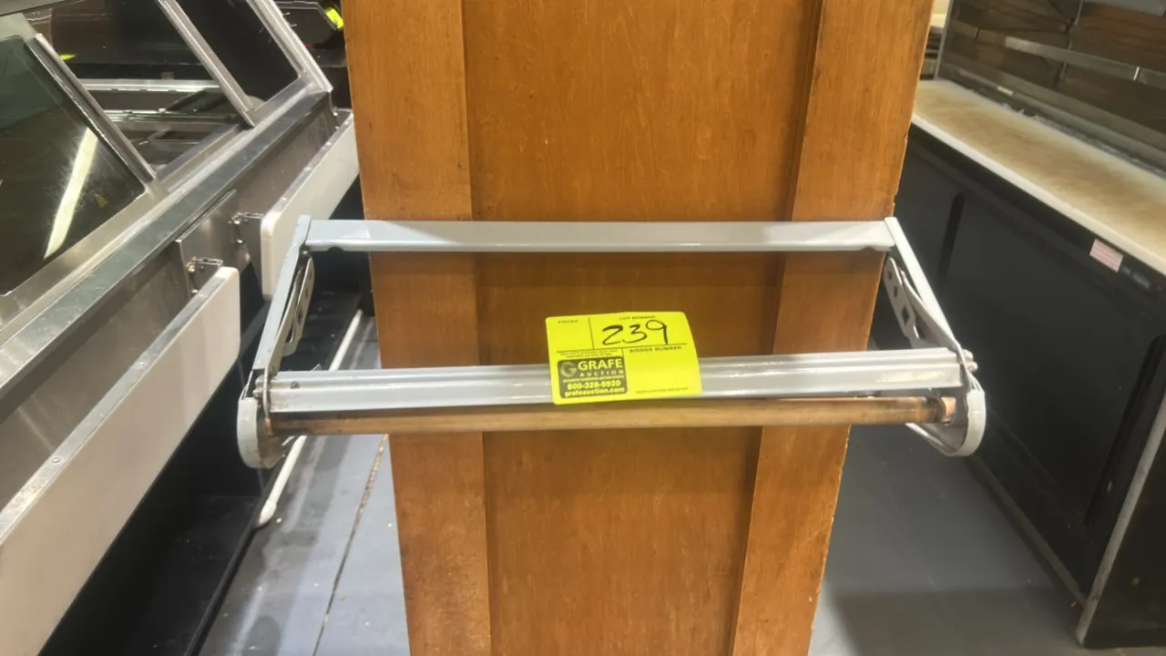 Paper roll dispenser. Features gray painted metal frame and spring-loaded cutter bar. Designed for wall or surface mounting. Wooden column and backgro