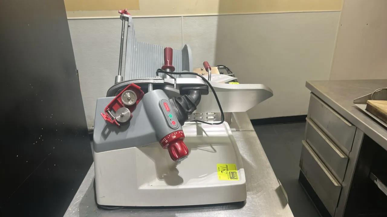 Berkel deli meat slicer. Features gravity-feed product carriage with meat pusher, adjustable slice thickness control knob, integrated top-mounted two-