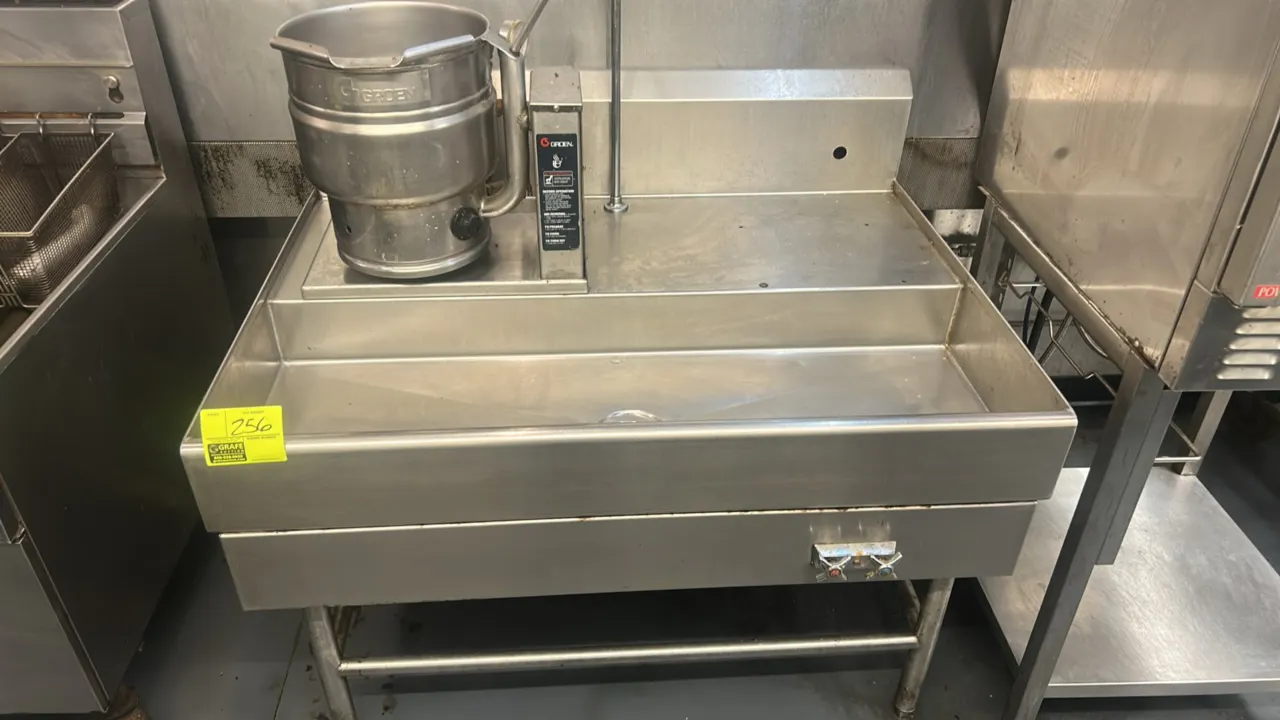 Groen tilting steam jacketed kettle with stainless steel draining table. Features stainless steel construction, manual tilt handle, pour spout, pressu