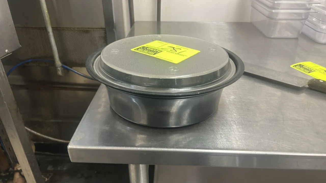 Round poly food storage container. Features black plastic construction with a clear plastic lid. Background items not included.