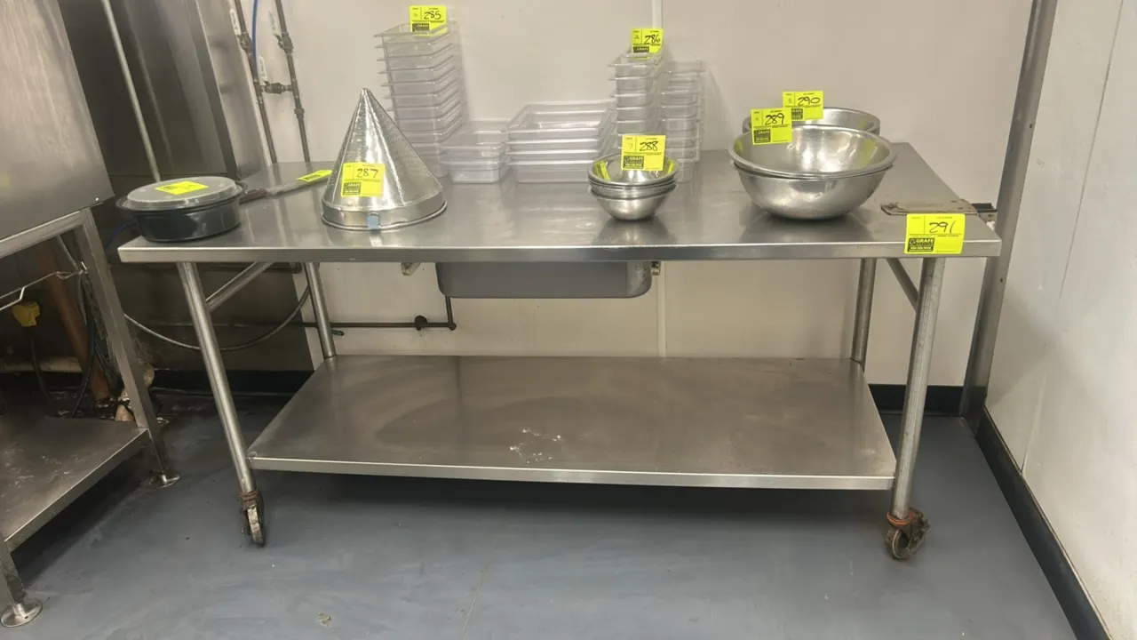 Stainless steel portable table. Features lower undershelf and underslung drawer. 72" x 30". Mounted on casters. Contents not included.