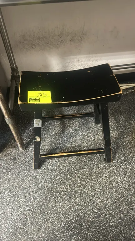 Laminate saddle seat stool. Features a curved seat, four-leg base, and integrated foot stretchers. Black finish.