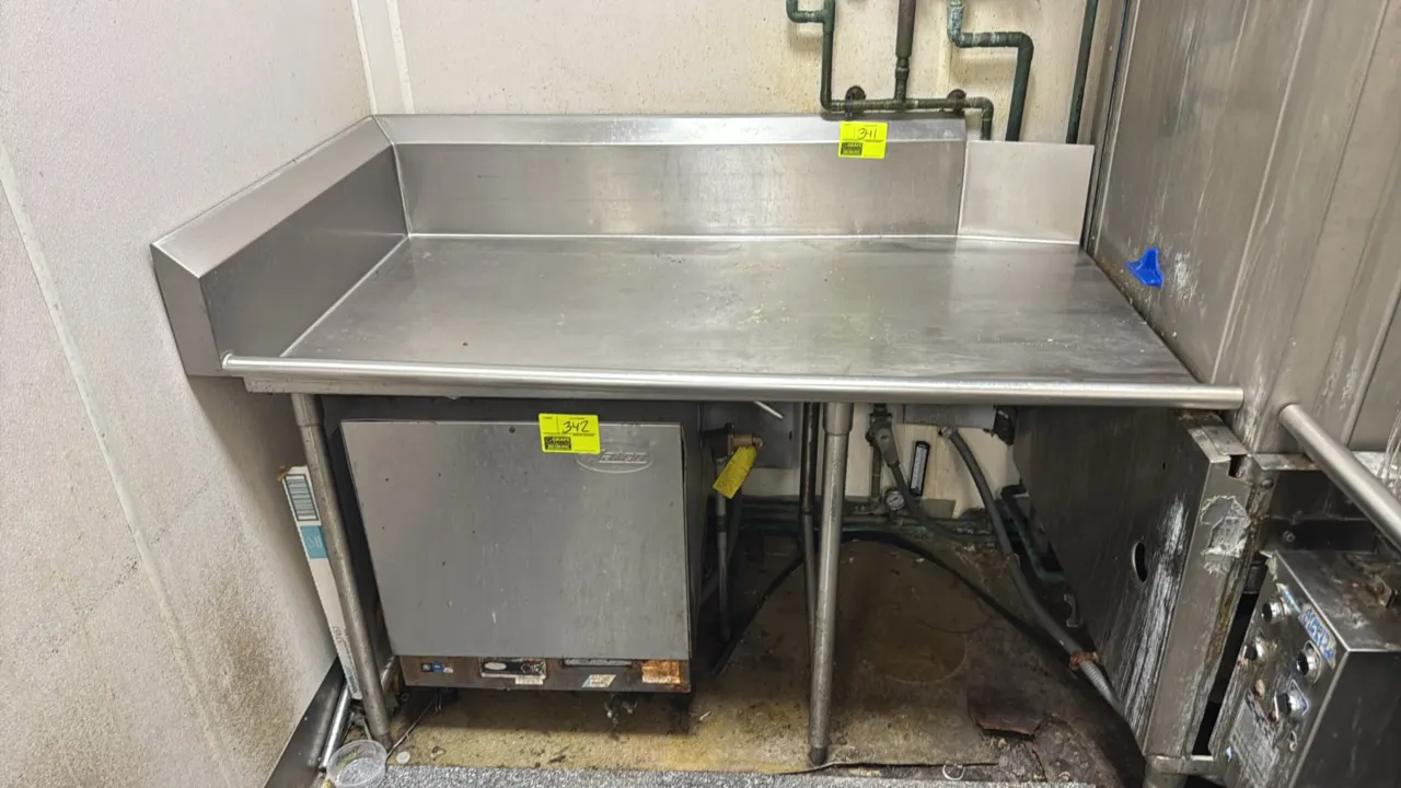 Stainless steel left-side drain table. Features rear backsplash, left end splash, and rolled front rim. Mounted on tubular stainless steel legs with a