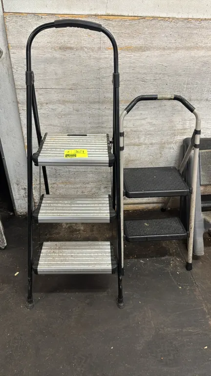 Folding step ladders. Includes (1) 3-step ladder with black metal frame and aluminum treads, and (1) 2-step ladder with light frame and textured steps