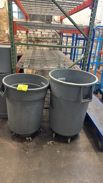 Rubbermaid Brute polyethylene trash cans. Features integrated side handles and durable plastic construction. Mounted on rolling dollies with swivel ca
