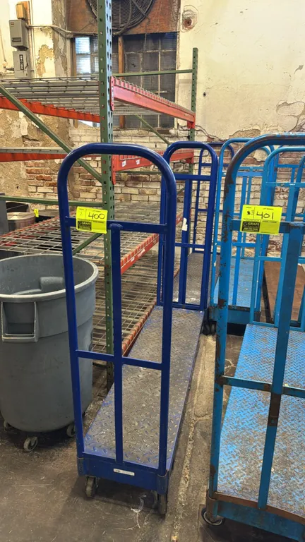Metal U-boat cart. Features blue diamond plate steel deck and dual removable tubular handles. 5'L. Mounted on casters. Racking and trash can in backgr