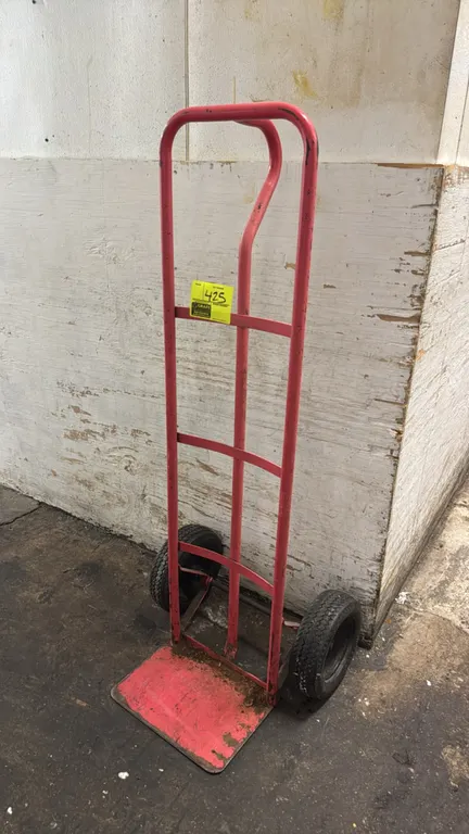 Metal 2-wheel hand truck dolly. Features red tubular steel frame, continuous loop handle, solid toe plate, and two pneumatic tires.