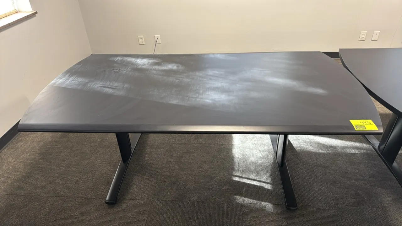 Laminated wood conference table. Features a dark laminate top with curved ends and beveled edges. Dimensions: 6'L x 3'W. Mounted on a black metal T-le