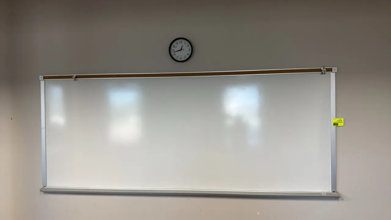 Dry erase whiteboard with wall clock. Features an aluminum frame, integrated top cork display strip with clips, and a full-length bottom marker tray.