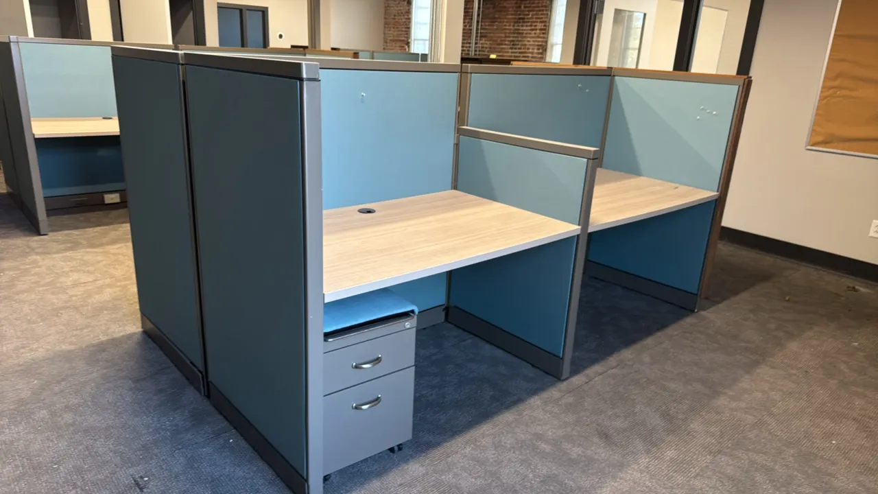 4-station cubicle workspace. Features light woodgrain laminate desks, blue fabric privacy panels, rustic wood plank end panels, and base raceway power