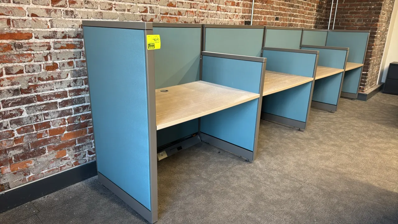 4-cubicle workspace system with desks. Features blue fabric-upholstered privacy panels with metal trim, light woodgrain laminate work surfaces, deskto