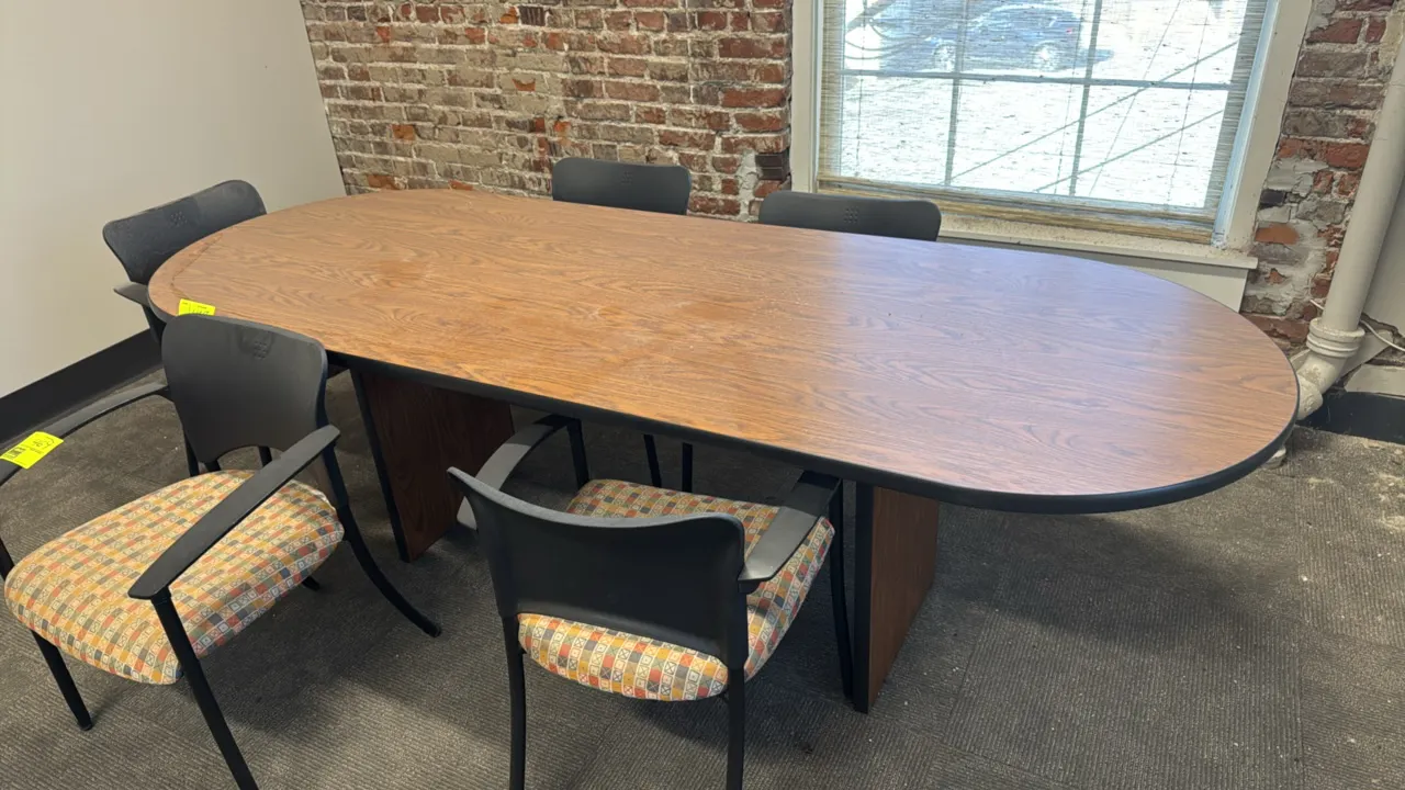Wood laminate conference table. Features a racetrack oval top with black bumper edge trim and dual panel slab base. Dimensions: 8'L x 2.5'W. Chairs no