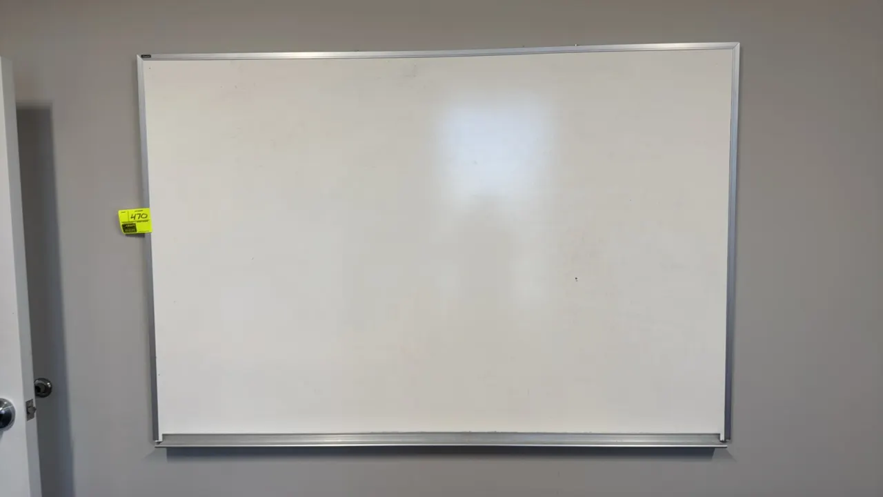 Dry erase board. Features an aluminum frame and an integrated bottom marker tray. Dimensions: 6' x 4'. Wall-mounted design.